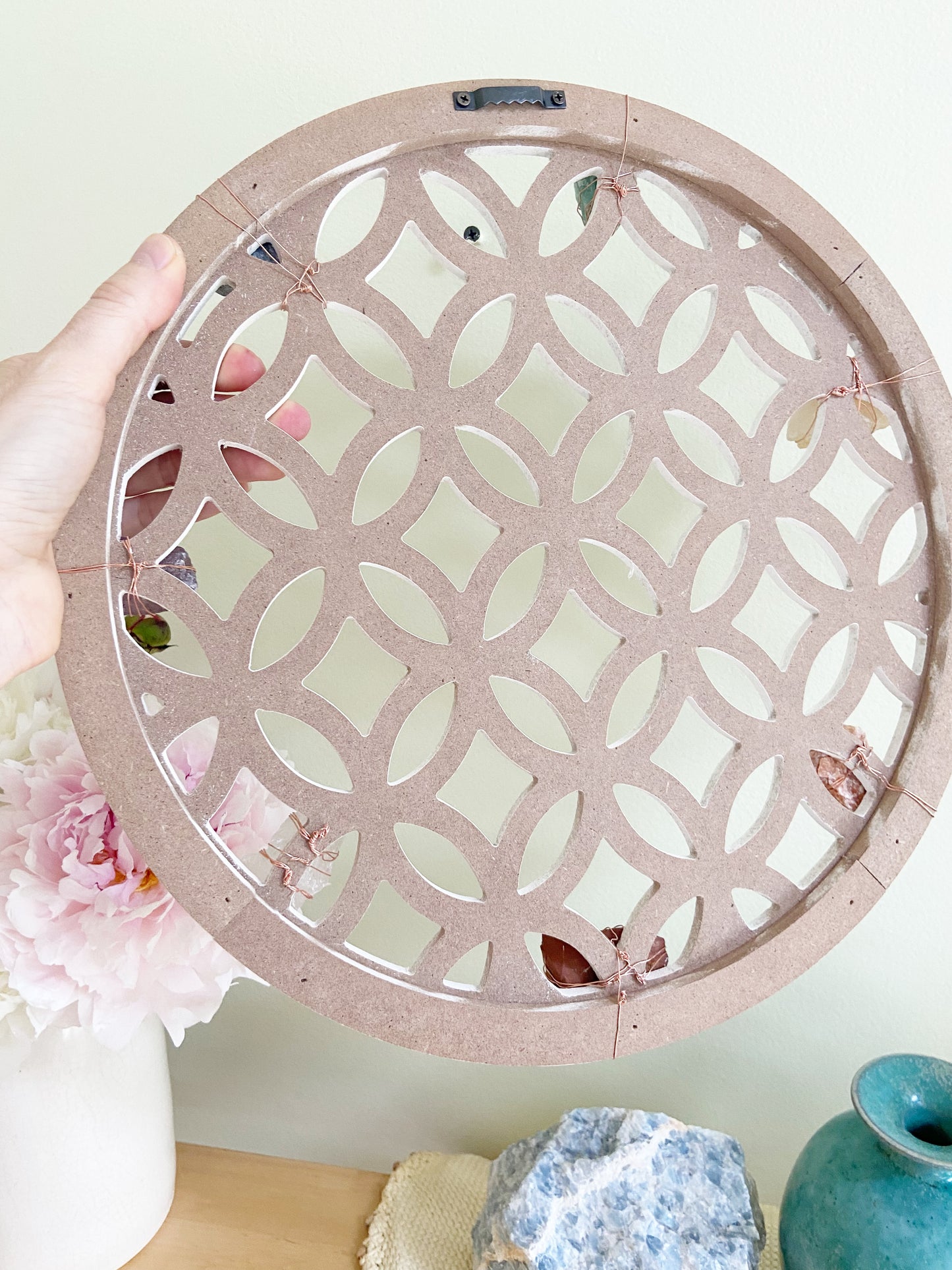 Decorative circular lattice panel held by a hand with flowers and vases in the background
