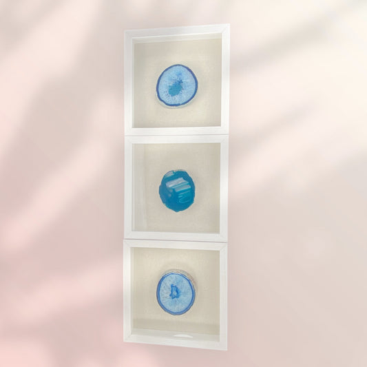 3 stacked white frames with linen backgrounds with one thick blue druzy agate in the center of each frame oriented vertically on a pink wall with shadows
