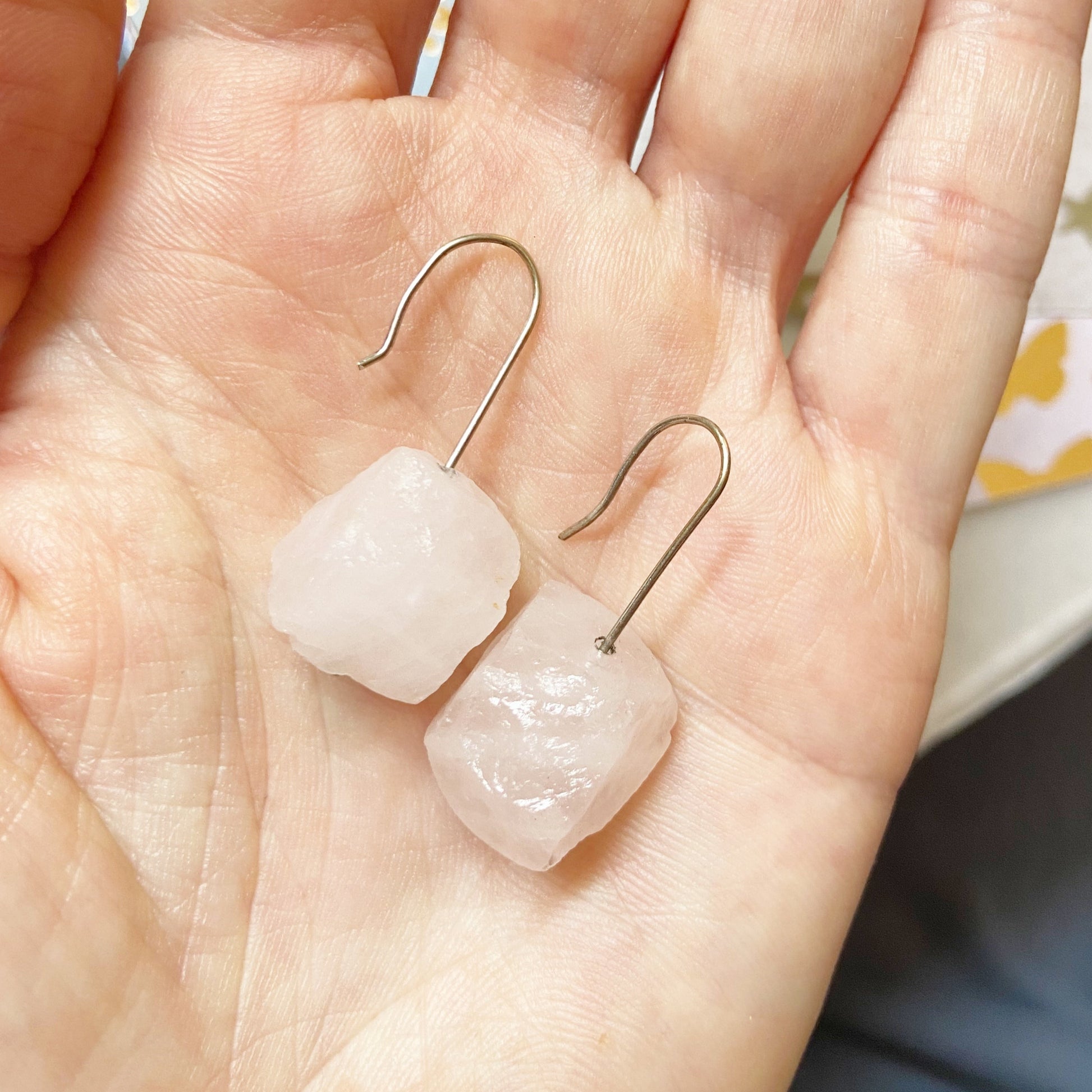 Pair of earrings with pinkish stones held in a hand against a blurred background