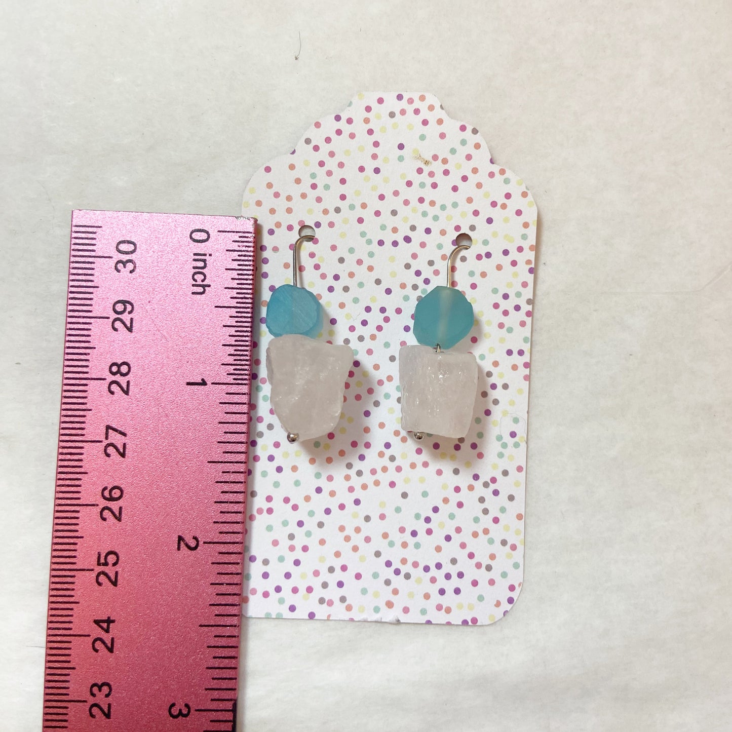 Pair of earrings on a polka dot card with a ruler for scale on a beige background