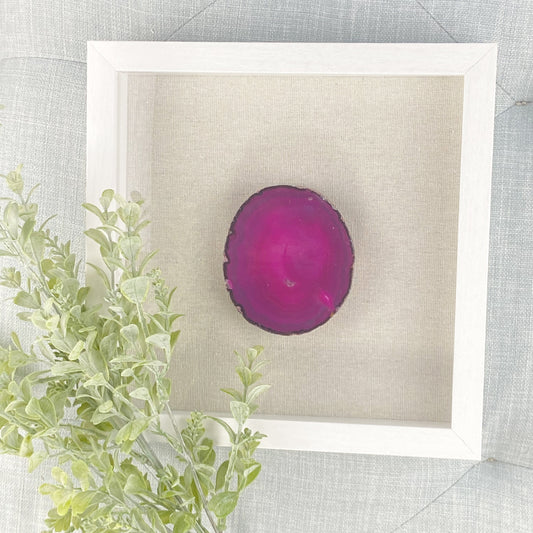 Framed pink agate stone on a textured surface with green leaves.