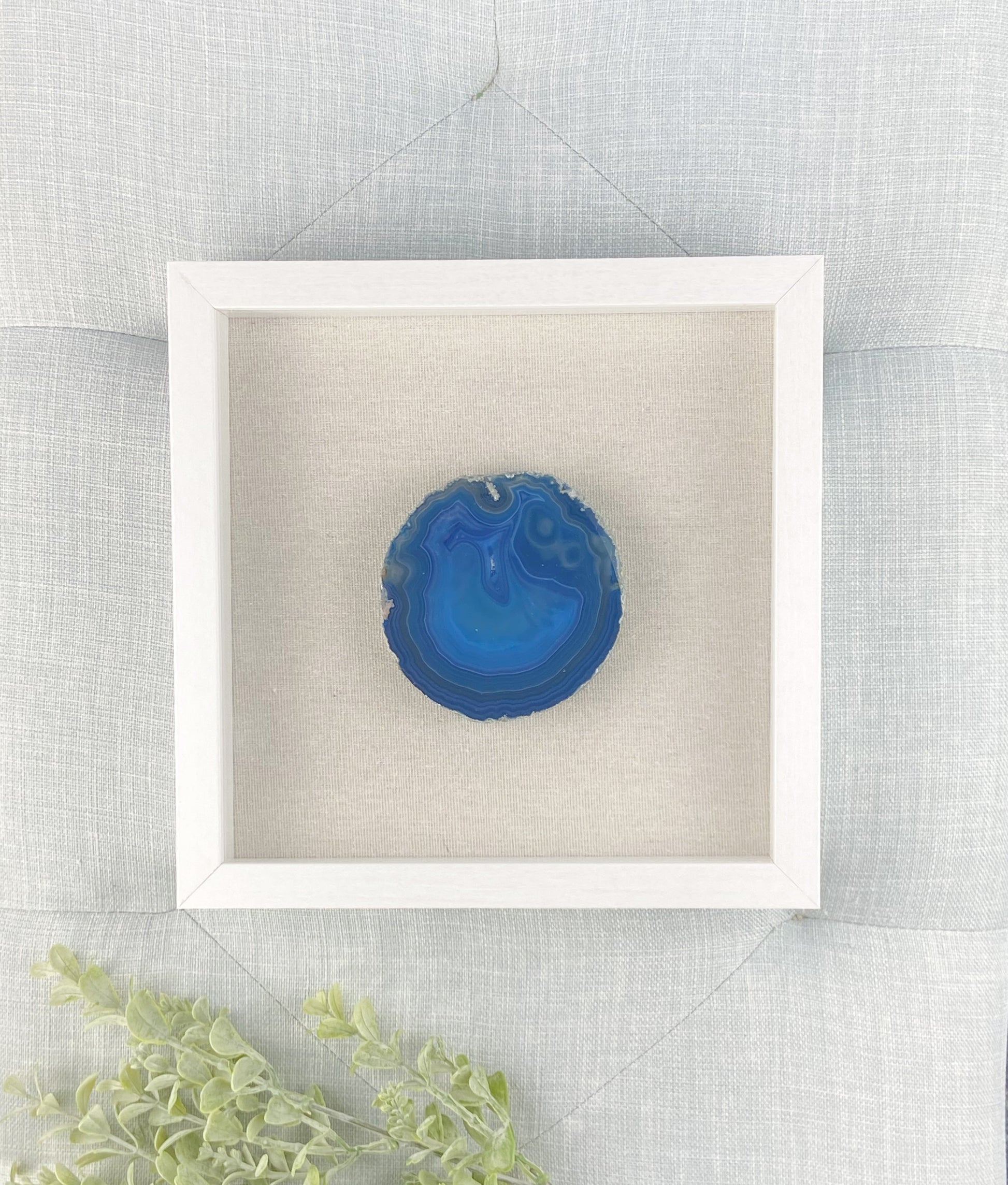 Blue decorative item in a white box on a textured surface with greenery.